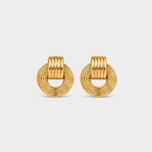 A pair of gold-toned hoop earrings with a textured, ridged circular design, shown on a light gray background.